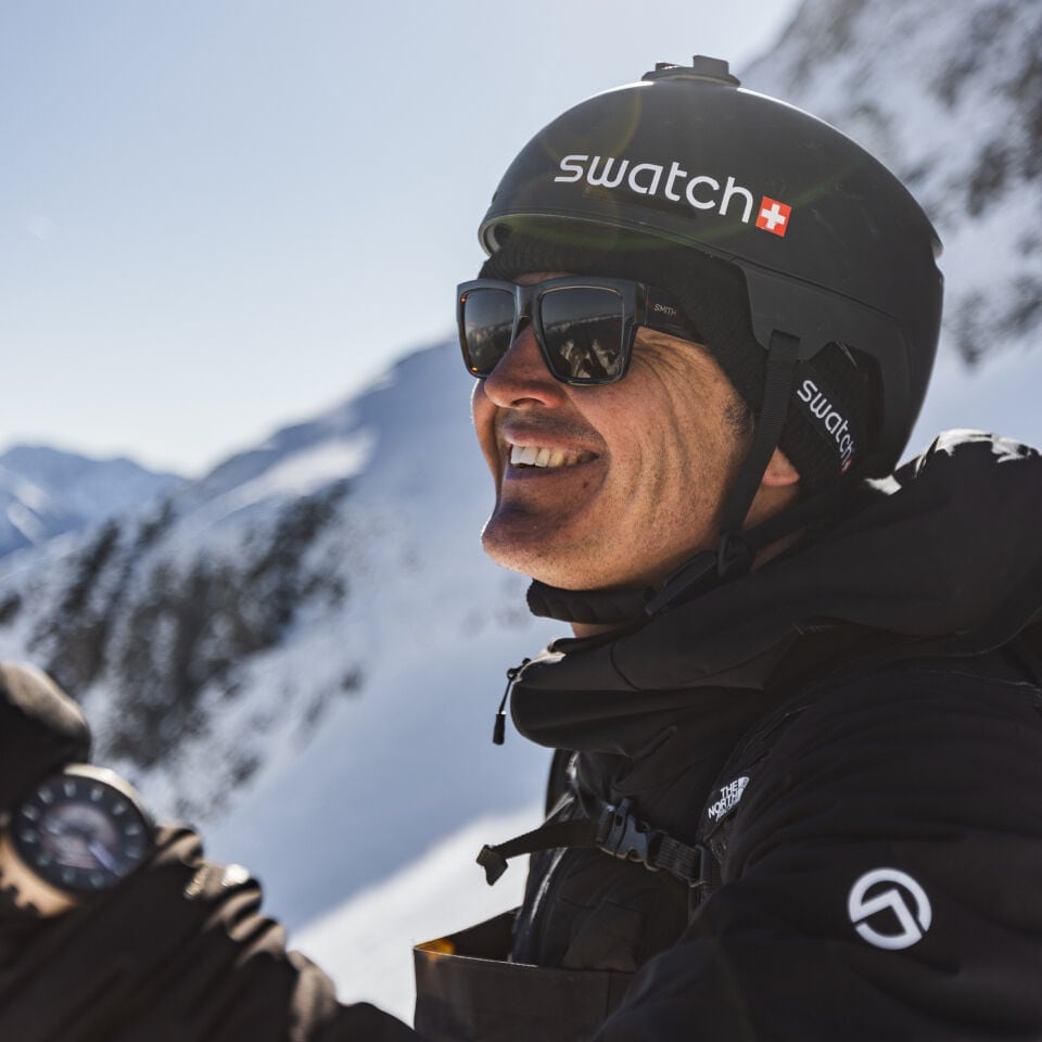 Portrait of Xavier De Le Rue smiling, wearing helmet and Swatch watch